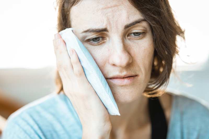 A woman holding her cheek in pain, indicating a toothache.
